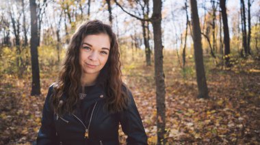 Güz ormanında poz veren güzel bir kadın. Deri ceketli kız ormanda yürüyor.