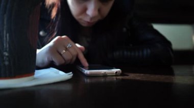 Bir kadın bir kafede otururken akıllı telefon kullanarak sosyal ağda bir kaseti çeviriyor. İnternette oturan kız telefonunu kullanıyor.