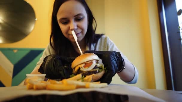 Un gros hamburger juteux avec deux morceaux, des légumes, de la sauce et des frites sur la table dans un café. — Video