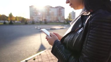 Genç bir kadın ayakta duruyor, dudaklarını büzüyor ve sosyal ağdaki çeşitli haberleri cep telefonuyla inceliyor..