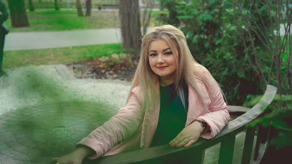 Een portret van een mooi meisje, zittend op een bankje bij de groene vegetatie. — Stockfoto