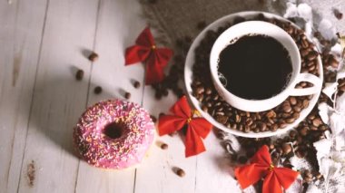 Bir fincan sıcak kahve, çörek ve kahve çekirdekleri masanın üzerinde. Lezzetli bir kahve ve tatlı bir atıştırmalık..