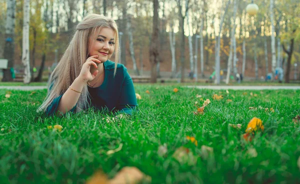 Çimlerin üzerinde yatan güzel bir kızın portresi. Büyüleyici bir kadın yeşil çimlerde yatıyor, sarı yapraklarla..