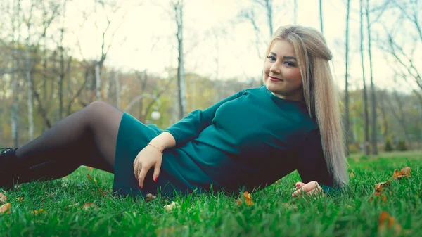 Un retrato de una guapa chica, acostada en la hierba. Una mujer encantadora se encuentra en la hierba verde con hojas amarillas.. — Foto de Stock