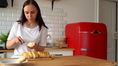 Genç bir kadın erimiş peynirden dilimlenmiş ekmek yayıyor sonra ısırıyor, mutfaktan zevk alıyor..