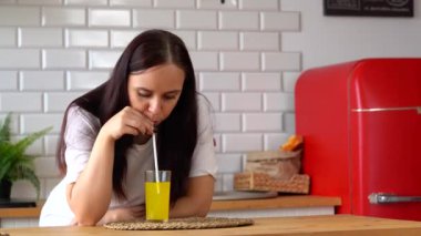 Mutfakta portakallı soda içen genç bir kadın. Karbonatlı limonatanın tadını çıkaran bir kadın samandan yudumluyor..