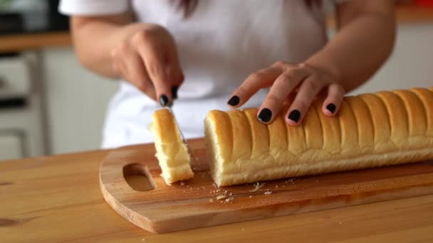台所の板にパンを切断する女性の閉じる 女性の手はキッチンテーブルの上にまな板にナイフでバゲットを切断 — ストック動画
