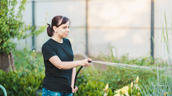 Woman watering the garden from hose. Female spraying water on vegetables with a garden hose. A happy woman with a hose takes care of the garden.