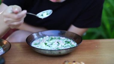 Soğuk çorba içen bir kadına yaklaş. Okroshka seven bir kadın, açık havada masada oturuyor..