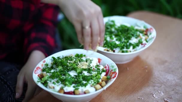 Kvinnan gör sallad utomhus. Närbild av kvinnors händer häller riven ost i tallriken. Tidsfrist. — Stockvideo