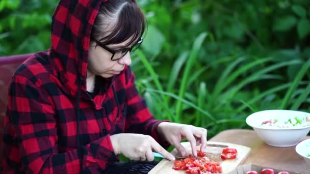 Молода жінка в окулярах ріже помідори на дерев'яній дошці на відкритому повітрі. Жіночий різання овоча з ножем на дошці . — стокове відео