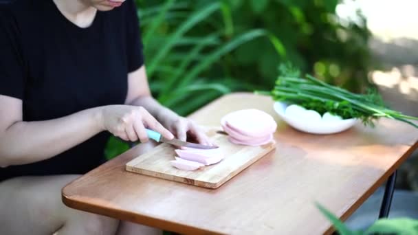 Mujer joven cortando salchichas en tablero de madera al aire libre. Mujeres manos corte productos de salchicha con cuchillo en la tabla de cortar . — Vídeos de Stock