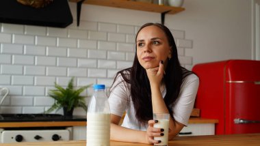 Genç bir kadın mutfakta süt içiyor. Yetişkin kadın kahvaltıda yararlı bir şeyler içiyor.