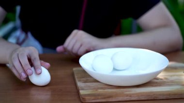 Kadın haşlanmış yumurta soyar, bahçede masada oturur. Kadın ellerini kapat, kabuktan tavuk yumurtası soy..