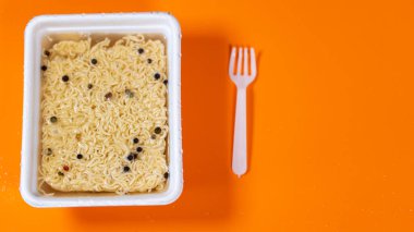 Portakal arkaplanlı soslu hazır erişteyi kapat. Sıcak su, makarna ve biberle tabağa dökülüyor..