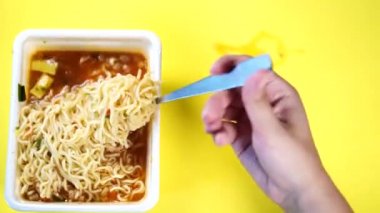 Sarı arka planda baharatlı hazır eriştelere yakın çekim yapın. Bir kadının eli çatalla makarna düzüyor..