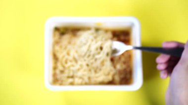 Sarı arka planda baharatlı hazır eriştelere yakın çekim yapın. Kadının eli makarnayla çatalı kaldırıyor..