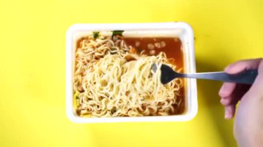 Sarı arka planda baharatlı hazır eriştelere yakın çekim yapın. Bir kadının eli çatalla makarna düzüyor..