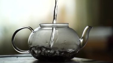 Sıcak su büyük şeffaf çaydanlığa dökülüyor. Kaynar suda demlenmiş çay yaprakları. Çay partisi kavramı.