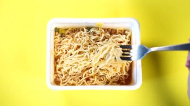 Sarı arka planda baharatlı hazır eriştelere yakın çekim yapın. Bir kadının eli çatalla makarna düzüyor..