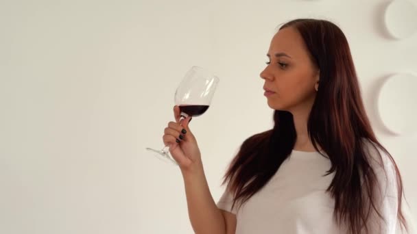 Mulher Jovem Olha Para Copo Vinho Bebe Contexto Parede Branca — Vídeo de Stock