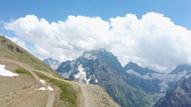 Bulutlu gökyüzüne karşı karlı dağ. Beyaz bulutların altından mavi gökyüzünde yüzen dağların üzerinden doğada güneşli bir günde karla kaplı.