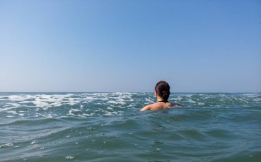 Siyah mayo giyen genç bir kadın denizde vakit geçiriyor. Yetişkin kadın dalgalara doğru yüzüyor.