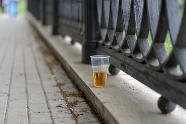 Close up of disposable cup with beer stands on concrete on waterfront. Alcoholic beverage forsaken in public park.
