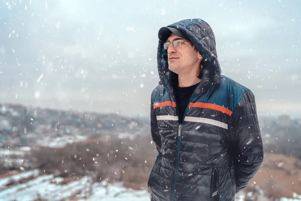 Взрослый Мужчина Капюшоне Очках Стоящих Падающим Снегом Окна Заката Зимней — стоковое фото