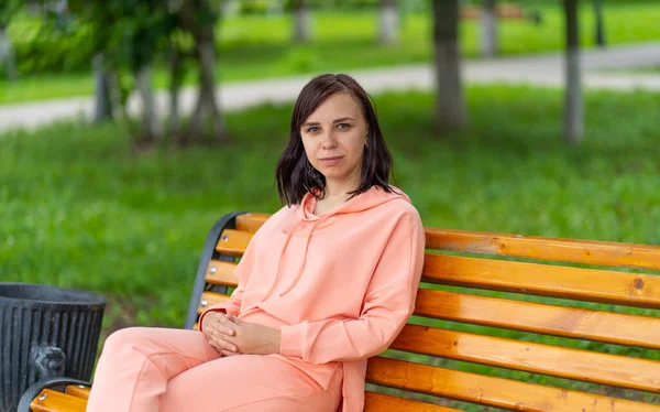 Young woman sits on bench in park. Adult female enjoys her rest on fresh air. — Stock Photo, Image