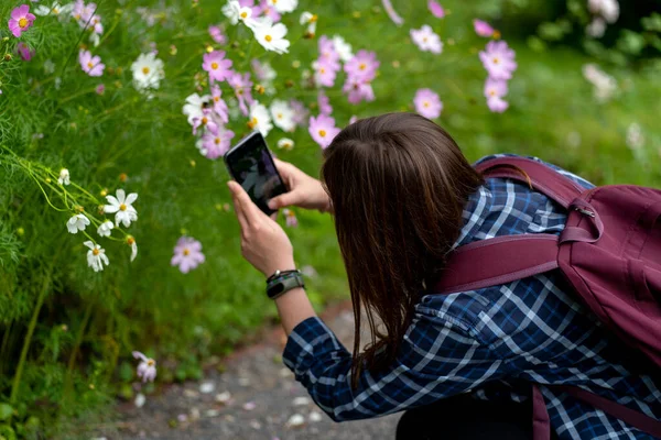 若い女性のクローズアップはスマートフォンで写真を撮ります 公園内の携帯電話で花を撮影する女性観光客 — ストック写真
