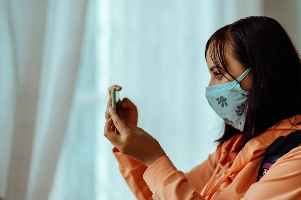 Крупный план молодой женщины в медицинской маске фотографирует на смартфоне. Фотография женщин-туристов на мобильном телефоне в общественных помещениях. — стоковое фото