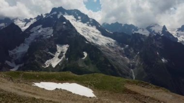 Bulutlu gökyüzüne karşı karlı dağ. Beyaz bulutların altından mavi gökyüzünde yüzen dağların üzerinden doğada güneşli bir günde karla kaplı.