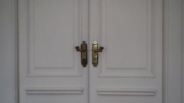 Kapalı, beyaz, çift kapılı bir kapının yakın çekimi. Kapıda altın kaplama kapı kolları var.