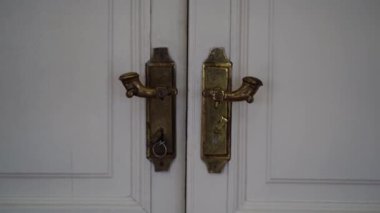 Kapalı, beyaz, çift kapılı bir kapının yakın çekimi. Kapıda altın kaplama kapı kolları var.