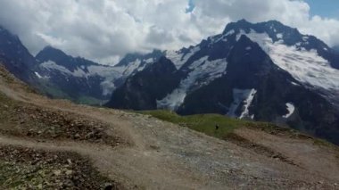Bulutlu gökyüzüne karşı karlı dağ. Beyaz bulutların altından mavi gökyüzünde yüzen dağların üzerinden doğada güneşli bir günde karla kaplı.