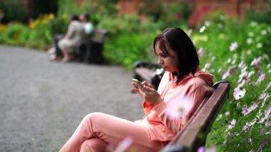 Yetişkin bir kadın parkta bankta akıllı telefon kullanıyor. 