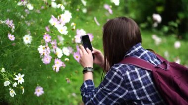 Genç bir kadın akıllı telefondan fotoğraf çekiyor. Kadın turist parkta cep telefonuyla çiçek fotoğrafı çekiyor..