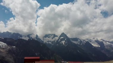 Bulutlu gökyüzüne karşı karlı dağ. Beyaz bulutların altından mavi gökyüzünde yüzen dağların üzerinden doğada güneşli bir günde karla kaplı.