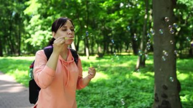 Genç esmer kadın, güneşli bir günde parkta dolaşır ve sabun köpüğü yapar..