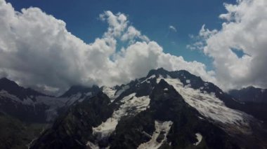 Bulutlu gökyüzüne karşı karlı dağ. Beyaz bulutların altından mavi gökyüzünde yüzen dağların üzerinden doğada güneşli bir günde karla kaplı.