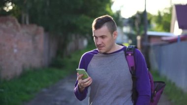 Yetişkin bir erkek, günlük giysiler içinde telefona cevap veriyor ve banliyö sokağının bulanık arka planında dikilirken gözlerini kaçırıyor.