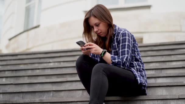 年轻女子坐在庄园的楼梯上 用智能手机播放新闻 王宫台阶上坐着带着手机的成年女性 — 图库视频影像