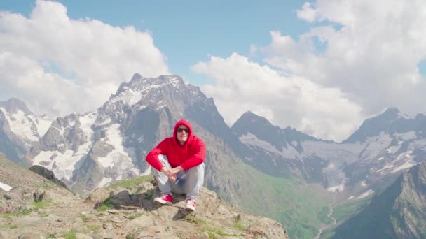 Jovem Homem Bonito Com Capuz Vermelho Sentado Frente Das Montanhas — Vídeo de Stock