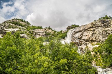 Taşrada güneşli bir yaz gününde kayalardan mavi gökyüzüne doğru akan hızlı su akıntısı.