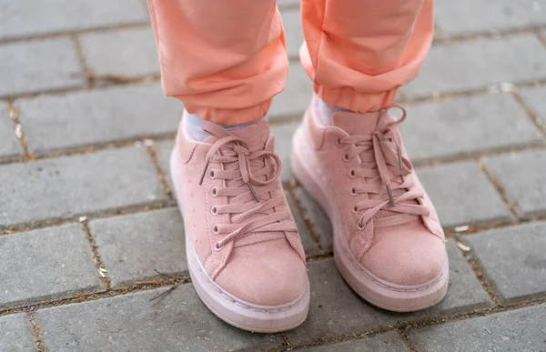 Woman in pink sneakers stands on paving slabs.