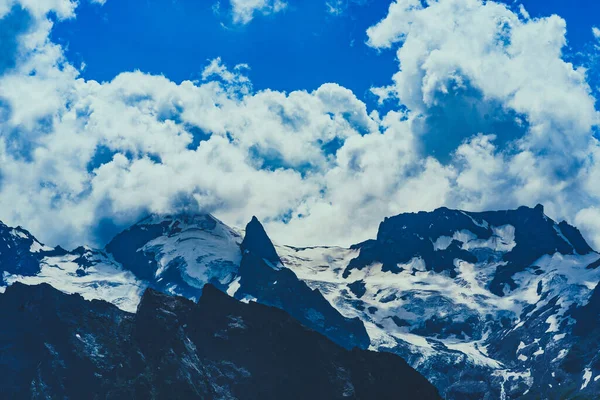 Beautiful mountain landscape in wooded area in summertime. Mighty mountains with snow and green array in cloudy weather.