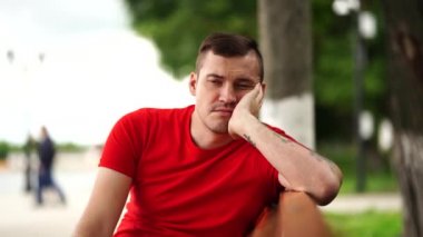 Kırmızılı sıkılmış genç adam bankta oturuyor. 