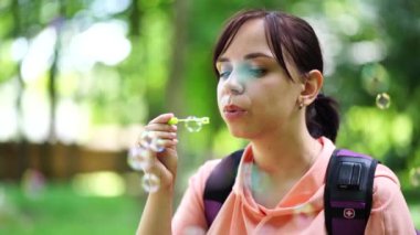 Genç esmer kadın, güneşli bir günde parkta dolaşır ve sabun köpüğü yapar..