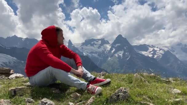 穿着红色帽衫的年轻英俊男子欣赏高山美景 — 图库视频影像